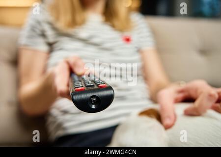 La femme tient la télécommande de la télévision. Femelle est assis sur le canapé dans le salon et changer les chaînes sur la télévision. Concept de divertissement et week-ends paresseux Banque D'Images