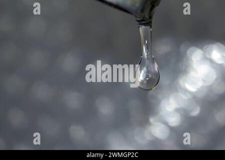 Détail de la petite goutte d'eau sortant du robinet goutte à goutte avec fond lumineux horizontalement Banque D'Images