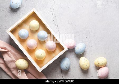 Plateau en bois avec des œufs de Pâques de couleur pastel avec des taches dorées et une serviette rose sur fond de béton avec espace de copie. Banque D'Images