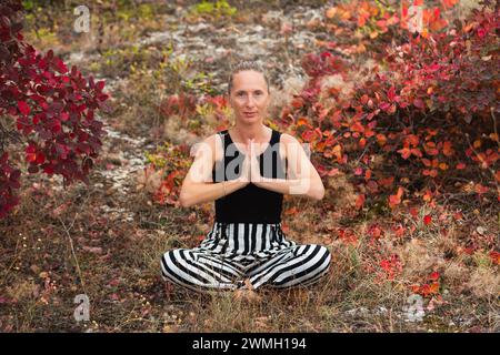 Une jeune femme adulte est assise dans la position de lotus sur un fond de verdure d'automne. Méditation idéale. Sport heureux Banque D'Images