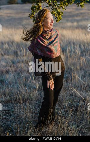 Portrait en pied dans les rayons d'un coucher de soleil. Femme caucasienne adulte avec un sourire réservé. Composition verticale Banque D'Images