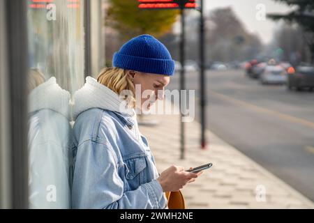Pensif hipster Guy attendant le transport de la ville à l'arrêt de bus, surfant sur Internet, lisant des nouvelles en ligne Banque D'Images