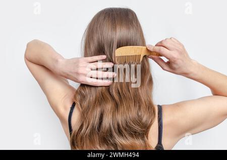 Femme peigne ses cheveux ondulés avec peigne en bois sur fond gris. Prend soin de cheveux sains et propres Banque D'Images