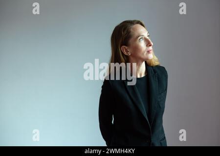 Portrait de profil d'une jeune femme attirante adulte dans un costume noir sur un fond blanc regardant avec intérêt. Banque D'Images