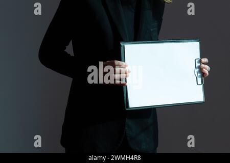 Une feuille de papier blanche sur une tablette d'écriture est illuminée par la lumière du soleil dans les mains d'une femme. Banque D'Images