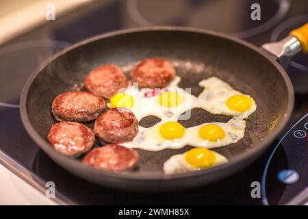 Des mini hamburgers grésillants et des œufs de caille cuisent sur une cuisinière. Banque D'Images