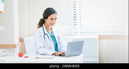 Belle et professionnelle femme médecin à l'aide d'un ordinateur portable, travaillant à son bureau dans le bureau du médecin. Banque D'Images