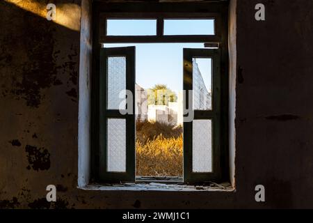 Fenêtre brisée endommagée donnant sur la cour à Al Jazirah Al Hamra ville abandonnée à Ras Al Khaimah, Émirats arabes Unis. Banque D'Images