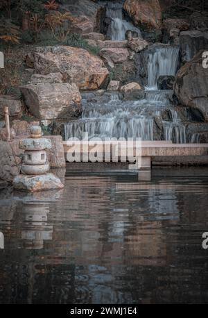 Lanterne décorative japonaise en pierre devant avec des érables orange et un pont. Cascade longue exposition cascade lisse soyeuse sur les falaises rocheuses dans Banque D'Images