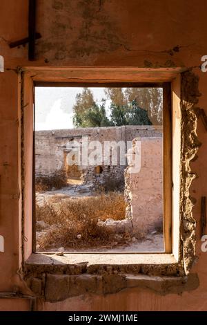 Vue à travers une fenêtre brisée de bâtiments en ruine et la cour dans la ville hantée d'Al Jazirah Al Hamra à Ras Al Khaimah, Émirats arabes Unis. Banque D'Images