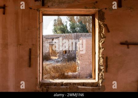 Vue à travers une fenêtre brisée de bâtiments en ruine et la cour dans la ville hantée d'Al Jazirah Al Hamra à Ras Al Khaimah, Émirats arabes Unis. Banque D'Images