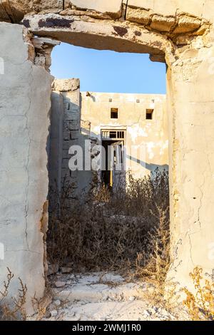 Bâtiments résidentiels en ruine, murs de briques démolis et cour couverte de végétation dans la ville hantée d'Al Jazirah Al Hamra à Ras Al Khaimah (Émirat arabe Uni) Banque D'Images