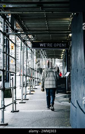 Un homme marchant le long du trottoir de Burrard Street, sous un échafaudage élevé pour des travaux de construction. Un panneau indique qu'un café est encore ouvert. Banque D'Images