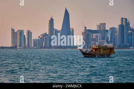 Doha, Qatar skyline de la rue corniche au coucher du soleil avec des boudins et des bateaux dans le golfe arabe Banque D'Images