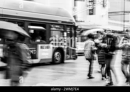 Vancouver, Canada - 21 février 2024 : scène en noir et blanc d'un bus et de gens traversant Georgia Street. La vitesse d'obturation lente a rendu leur mouvement flou. Banque D'Images