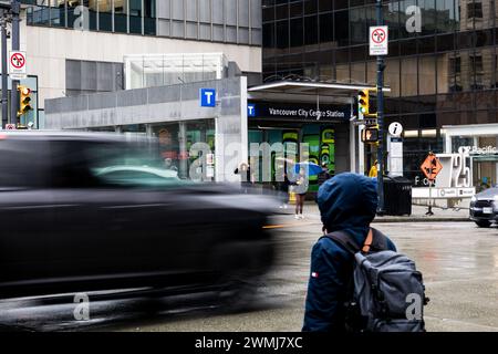 Vancouver, Canada - 21 février 2024 : une personne attend de traverser Georgia Street, avec une voiture qui passe, son mouvement brouillé par la vitesse d'obturation lente. Banque D'Images