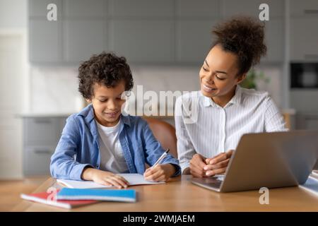 Mère noire aide son fils avec les devoirs à la table de la cuisine Banque D'Images