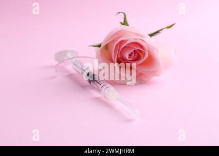Cosmétologie. Seringue médicale et fleur de rose sur fond rose, gros plan Banque D'Images
