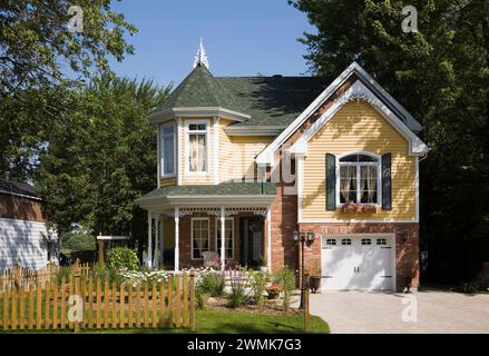 Maison de style victorien à deux étages en briques rouges et en claquettes jaunes avec jardin paysager et allée en pierre pavée en été. Banque D'Images