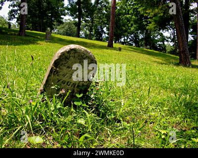 Vieille pierre tombale penchée sur une colline herbeuse Banque D'Images