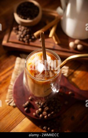 Café glacé servi dans une tasse en verre à double paroi et paille de métal, une boisson fraîche d'été préparée avec des glaçons et des épices, cannelle, muscade, vanille, mu Banque D'Images