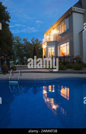 Maison moderne de deux étages avec bardage Havane avec jardin paysagé et piscine creusée illuminée au crépuscule. Banque D'Images