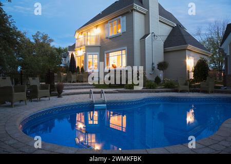 Maison moderne de deux étages avec bardage Havane avec jardin paysagé et piscine creusée illuminée au crépuscule. Banque D'Images