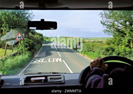 Vue d'une voiture d'une route marquée avec le mot 'slow' et la campagne anglaise environnante ; Grande-Bretagne Banque D'Images