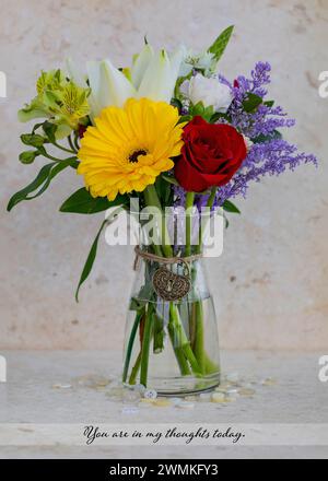 Petit bouquet coloré dans un vase en verre avec un message réfléchi dans le texte et un charme décoratif en forme de cœur noué autour du cou ; Studio shot Banque D'Images