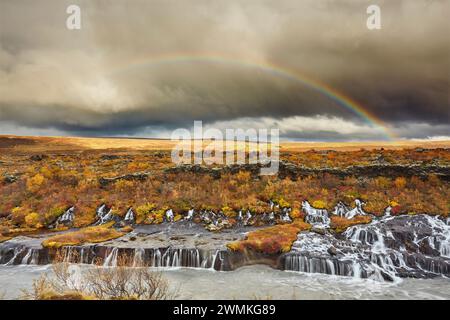 Hraunfossar Falls et un arc-en-ciel dans le ciel sous les nuages orageux, près de Reykholt, dans l'ouest de l'Islande ; Islande Banque D'Images