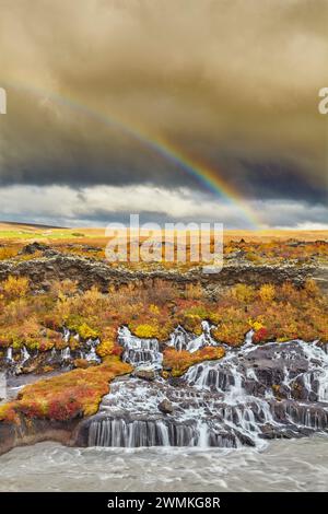 Hraunfossar Falls et un arc-en-ciel dans le ciel sous les nuages orageux, près de Reykholt, dans l'ouest de l'Islande ; Islande Banque D'Images