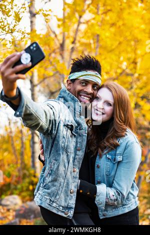 Gros plan d'un couple marié de race mixte prenant un selfie ensemble, souriant à la caméra du téléphone portable, passant du temps de qualité ensemble pendant un fam d'automne... Banque D'Images