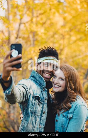 Gros plan d'un couple marié de race mixte prenant un selfie ensemble, souriant à la caméra du téléphone portable, passant du temps de qualité ensemble pendant un fam d'automne... Banque D'Images