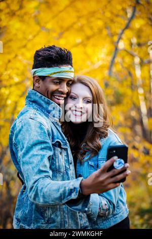 Gros plan d'un couple marié de race mixte prenant un selfie ensemble, souriant à la caméra du téléphone portable, passant du temps de qualité ensemble pendant un fam d'automne... Banque D'Images