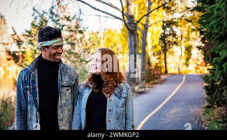 Gros plan d'un couple de races mixtes souriant et se regardant, marchant sur une route et passant du temps de qualité ensemble lors d'un automne famille outi... Banque D'Images