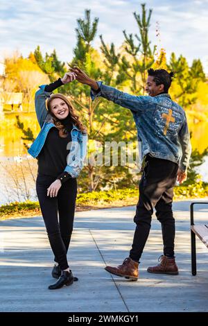 Un couple de courses mixtes dansant et s'amusant tout en passant du temps de qualité ensemble lors d'une sortie en famille d'automne dans un parc de la ville ; Edmonton, Alberta, Canada Banque D'Images