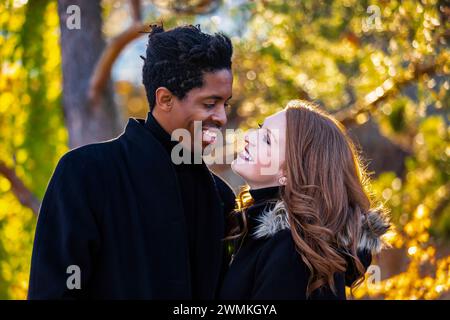 Portrait rapproché d'un couple de races mixtes souriant l'un à l'autre, passant du temps de qualité ensemble lors d'une sortie en famille d'automne dans un parc de la ville Banque D'Images