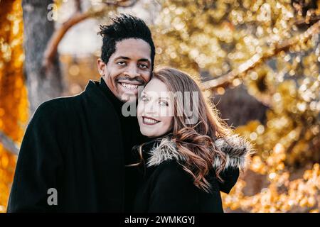 Portrait rapproché d'un couple de races mixtes souriant à la caméra, passant du temps de qualité ensemble lors d'une sortie en famille d'automne dans un parc de la ville Banque D'Images