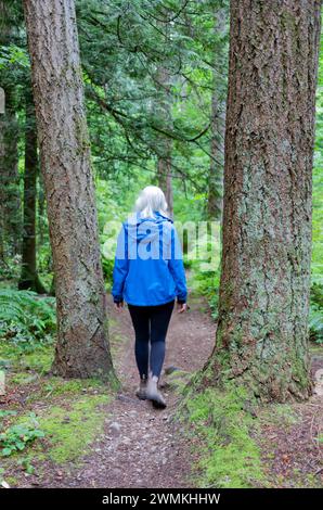 Vue prise de derrière d'une femme marchant le long d'un chemin de terre à travers Watershed Forest Trail ; Delta, Colombie-Britannique, Canada Banque D'Images