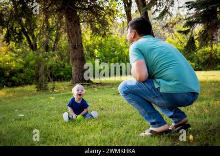 Père passant du temps de qualité et lançant une balle avec son jeune fils atteint du syndrome de Down, dans un parc de la ville pendant un chaud après-midi d'automne Banque D'Images