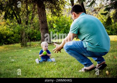 Père passant du temps de qualité et lançant une balle avec son jeune fils atteint du syndrome de Down, dans un parc de la ville pendant un chaud après-midi d'automne Banque D'Images