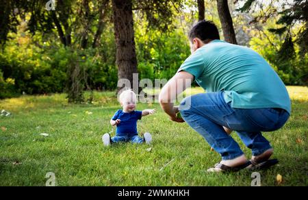 Père passant du temps de qualité et lançant une balle avec son jeune fils atteint du syndrome de Down, dans un parc de la ville pendant un chaud après-midi d'automne Banque D'Images