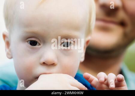 Portrait en gros plan d'un jeune garçon atteint du syndrome de Down, avec son père à l'arrière-plan ; Leduc, Alberta, Canada Banque D'Images