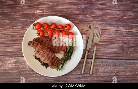 Deux médaillons de betterave grillée, un brin de tomates cerises, un bouquet de romarin et de grains de poivre noir sur une plaque ronde en céramique, à côté d'une fourchette et Banque D'Images