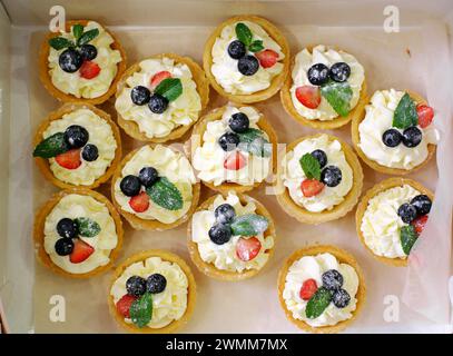 Une collection de tartelettes dorées garnies de crème au mascarpone, décorées de fraises fraîches, de bleuets et de feuilles de menthe. Vue de dessus Banque D'Images