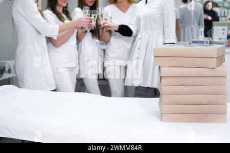 Collègues médicaux en uniformes blancs toast avec des verres à champagne, axé sur les boîtes de restauration pour une occasion de bureau festive, avec un espace pour le texte, idéal Banque D'Images