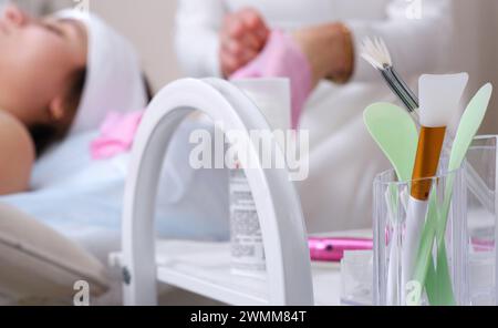 Un ensemble d'outils de cosmétologie est concentré au premier plan en arrière-plan, un cosmétologue met des gants, se préparant à servir un client. Banque D'Images