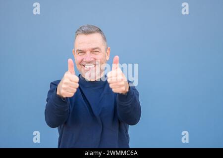 Gros plan d'un homme d'âge moyen attrayant motivé et enthousiaste donnant un geste d'approbation et de succès avec un sourire rayonnant Banque D'Images