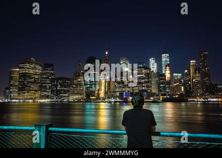 Un jeune homme regardant la vue de Manhattan Skyline de Brooklyn la nuit - New York City, USA Banque D'Images