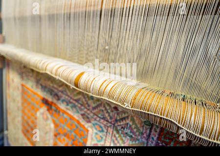 Un tapis traditionnel étant tissé sur un métier à tisser vertical de tapis, montrant la laine velours sous tension, fondation, chaîne et trame. fils sur un métier à tisser en gros plan. Banque D'Images